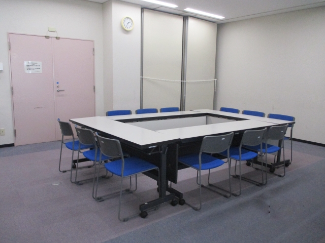 長机を四角く囲みその周りに椅子を12脚並べた会議室 半室を写した写真