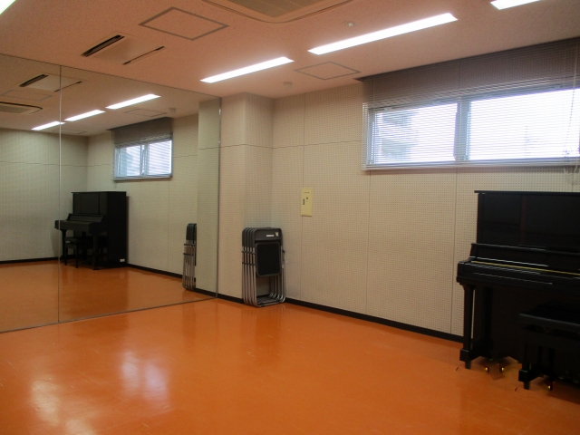 アップライトピアノと一面の鏡張りが写っているリハーサル室の写真