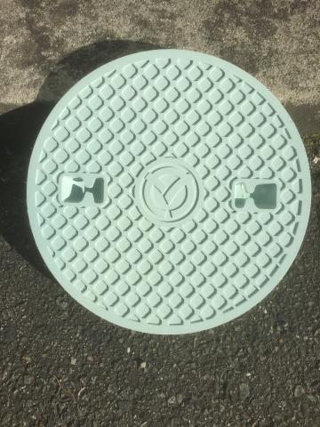 三田市章が刻印されたミントグリーン色の公共マスの蓋の写真