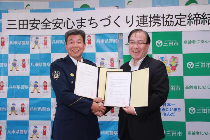 三田警察署長と三田市長が協定書を手に持ち笑顔で握手をしている写真