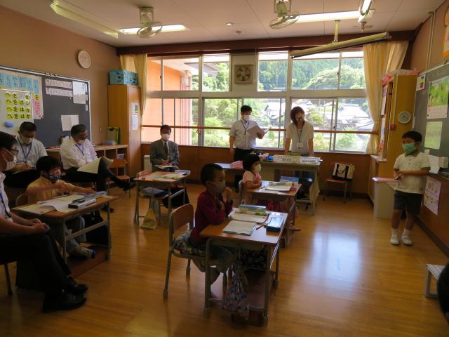 教室で子どもたちが机に座り、黒板の前で生徒の一人が立って説明している様子の写真