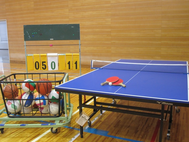 卓球台、ボール各種、得点板を写した多目的ホールの写真