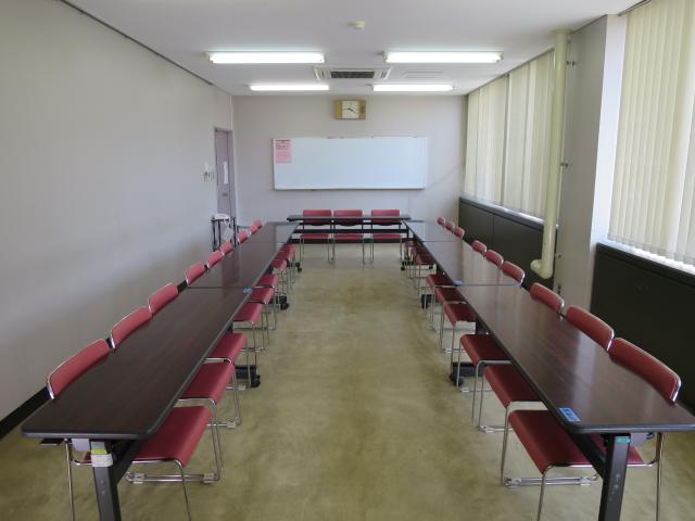ホワイトボードに向かって左手にドア、右手に窓、長机をUの字にして椅子を並べた研修室を写した写真