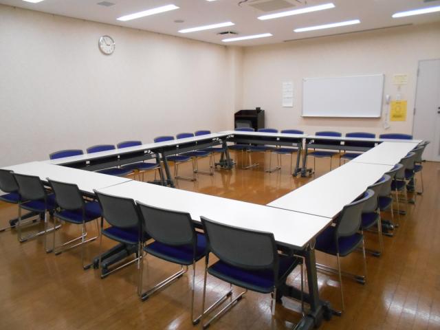 奥にホワイトボード、手前にテーブルを四角く囲みその周りに椅子を並べた様子を写した研修室の写真