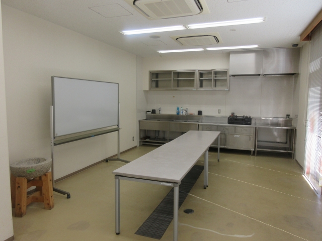 右手にホワイトボード、左手に長机が置かれた実習室(調理室)を写した写真