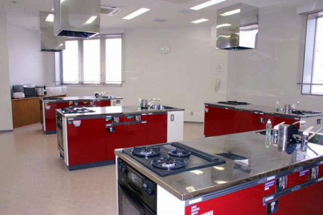流し台、ガスレンジ台付きの調理台4台が写った調理実習室の写真