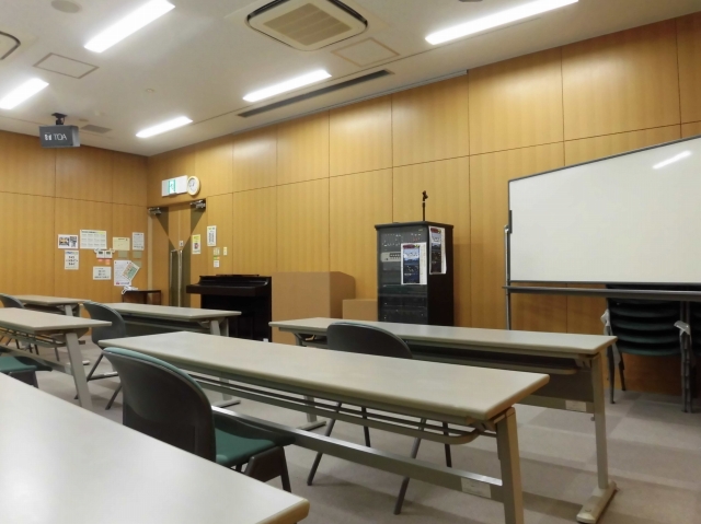 奥にホワイトボードと演台、手前にテーブルと椅子が並べられた大会議室(前室)を後方から写した写真