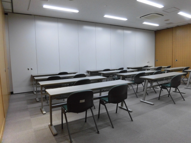 奥がパーテーションで区切られ、中央にテーブルと椅子が並べられた大会議室(後室)を後方から写した写真