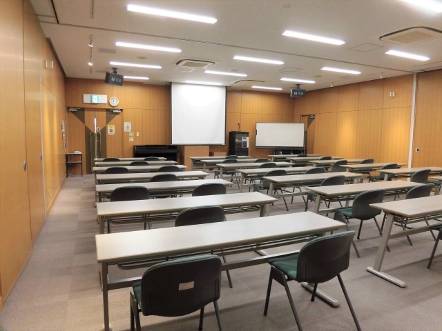 手前に長机と椅子、中央奥にスクリーン、右手奥にホワイトボードがある大会議室(全室)を後方から写した写真
