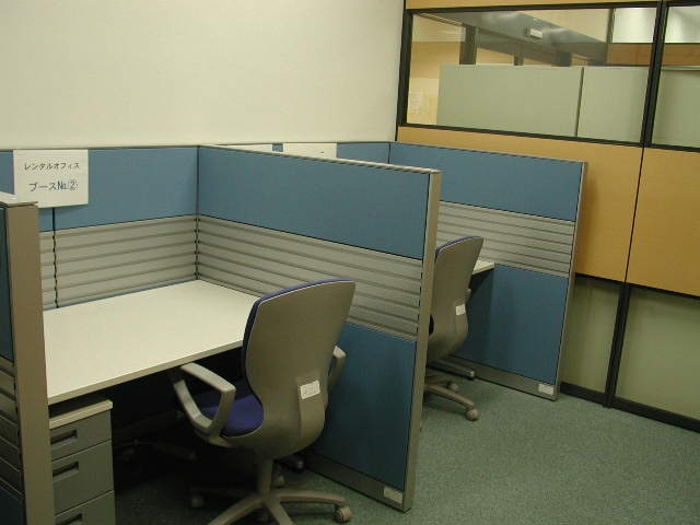 低い壁に囲われたキャビネット付きの事務机と椅子を写したレンタルオフィスの写真