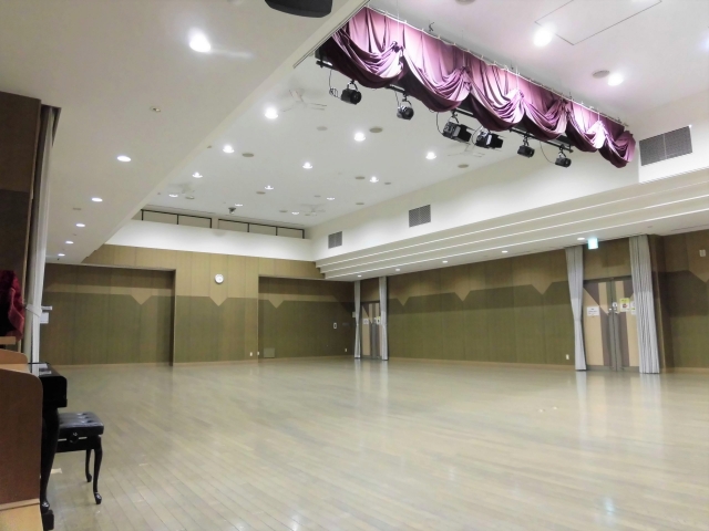 左手手前にアップライトピアノ、中央に照明がある多目的ホールを斜め前方から写した写真