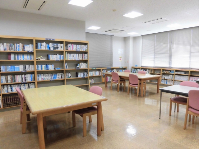 左手前に高い本棚、奥に低い本棚、手前に机と椅子が配置された図書コーナーの写真