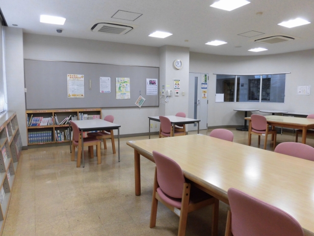 左手に低い本棚、右手と中央に机と椅子が配置された図書コーナーの写真