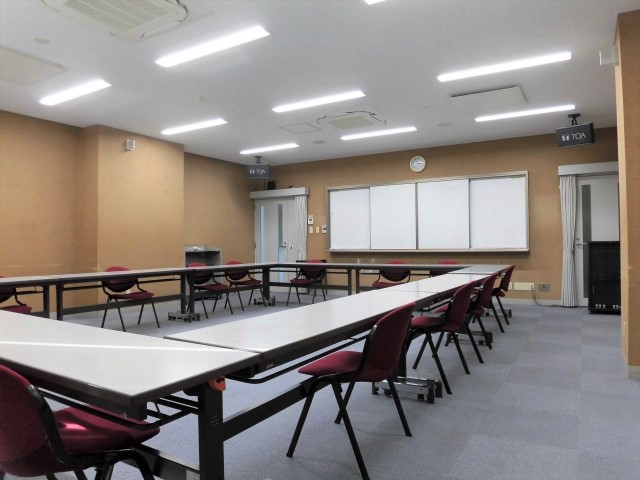 奥にスクリーン、手前にテーブルを四角く囲みその周りに椅子を並べた様子を写した中会議室の写真