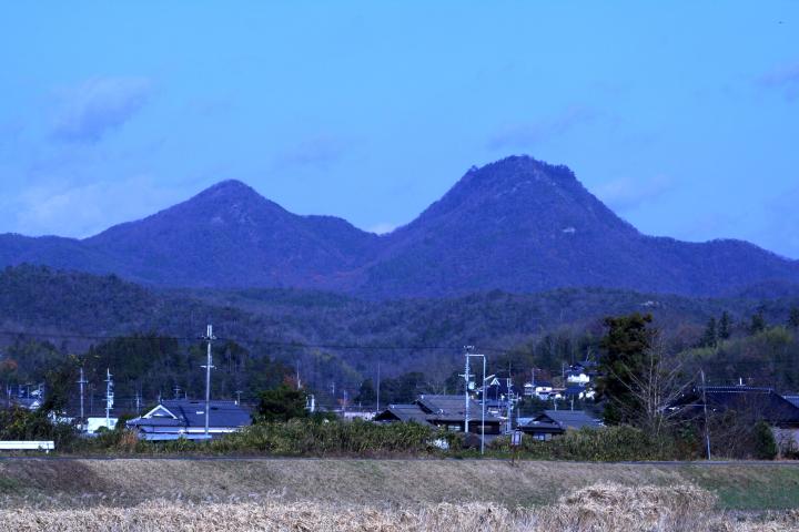青空の下、奥に二つの山が並んで見える田園風景の写真