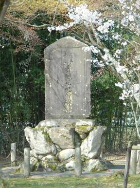 桜の木の下に、大きな石を土台にして記念碑が建っている写真