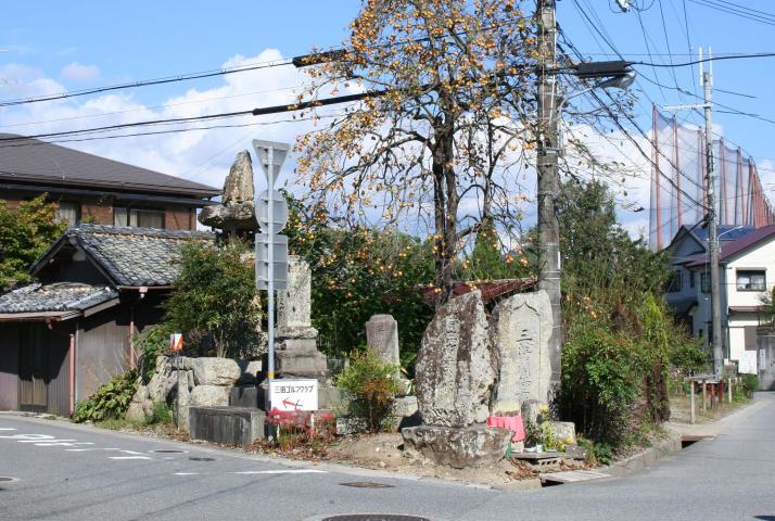 花の咲いた木の下に、いくつかの石碑が建っている交差点の写真