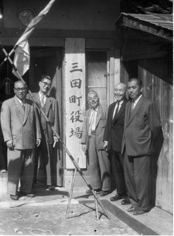三田町役場の看板が出ている建物入口で並んで記念撮影をする旧町村長らの写真