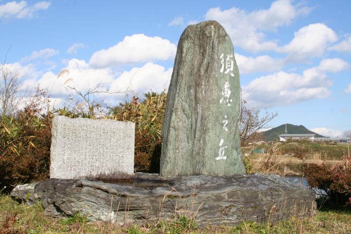 青空の下、石碑がそびえる丘の写真