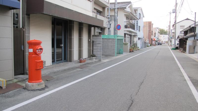 商店街の道沿いに設置されている丸型ポストの写真