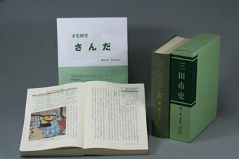 ページが開かれた本と、閉じてカバーに収納された本を並べた「三田市史第1巻」の写真