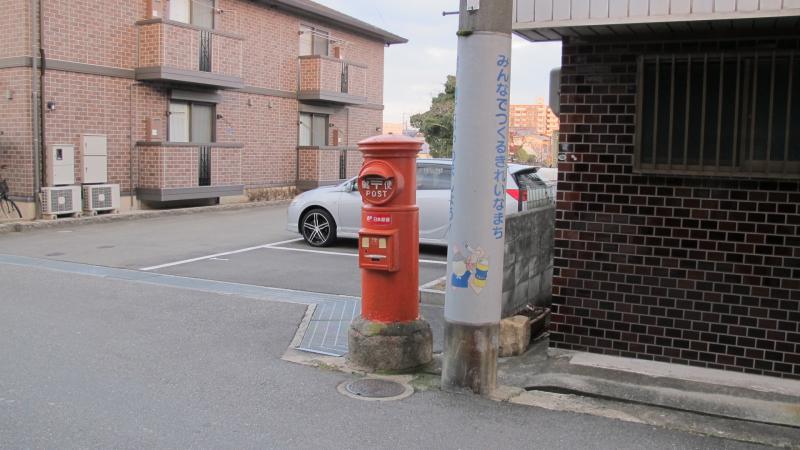 駐車場と電柱のすぐ傍に設置されている丸型ポストの写真