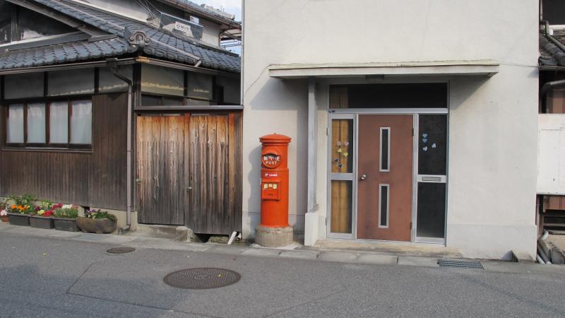 家屋の扉のすぐ近くに設置されている丸型ポストの写真