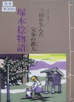 屋外でしゃがんで計器を弄る男性の絵が掲載された「塚本稔物語」の表紙