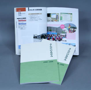 カラーページの見開きと表紙を並べて置かれた「さんだのあゆみ1998-2008」の見本写真