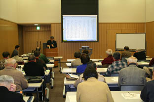 スクリーンのある会場内で着席して講座を受講する参加者たちの写真
