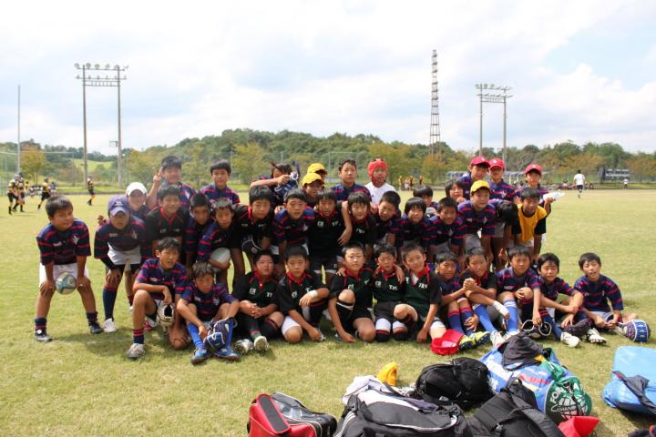 三田市ラグビーフットボール協会のチームメンバーがグラウンドに集まって記念撮影をしている写真