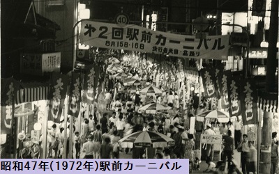 歩行者天国になった道を埋め尽くす人々の上に飾られた横断幕や出店が並ぶ昭和47年の駅前カーニバルの様子を撮影した白黒写真