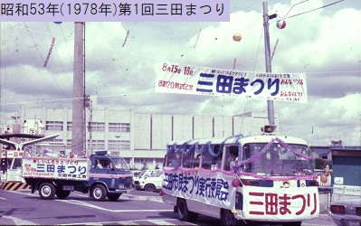 昭和53年の第1回三田まつりで上空にアドバルーンが浮かぶ中おこなわれた花車パレードと花車の上に掲げられた紺色の文字で大きく三田まつりと書かれた横断幕の写真