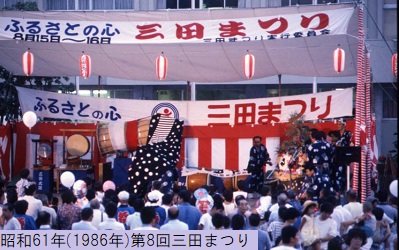 昭和61年におこなわれた第8回三田まつりのふれあいステージに掲げられた横断幕の下に置かれた様々な種類の太鼓を観客の背中側から撮影した写真