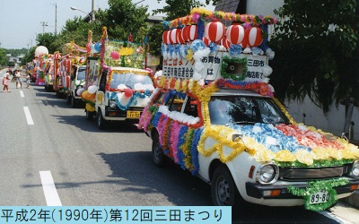 平成2年の第12回三田まつりでペーパーフラワーや提灯などで飾られた花車が縦一列に並びパレードをおこなっている様子を撮影した写真