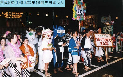 平成8年におこなわれた第18回三田まつりの市民総踊りに浴衣姿や仮装姿で参加する人々が白線の後ろで横に並んでいる写真