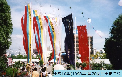 平成10年におこなわれた第20回三田まつりで披露された右から赤色と紺色および白黄水赤の幟がひとつになった三輪地区の幟さしの写真