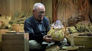 三田市の伝統工芸品三田鈴鹿竹器をあぐら姿で一つ一つ手作りしている老年の男性職人の写真