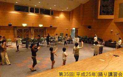 平成25年の第35回三田まつりに向けて屋内で右手を直角に挙げ左手を真っ直ぐ伸ばして踊りの講習会をおこなう人々の写真