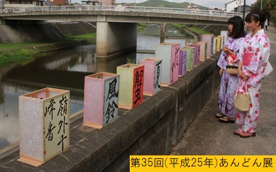 平成25年におこなわれた第35回三田まつりで橋の欄干の上に飾られた表面に墨で文字が書かれたあんどんを眺める浴衣姿の少女2人の写真