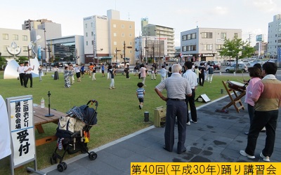 平成30年の第40回三田まつりに向けて芝生の上で踊りの講習会をおこなう人々とその様子を見守る人々の写真