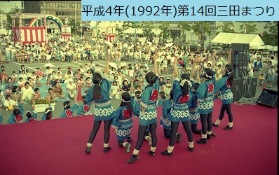 平成4年の第14回三田まつりのこどもステージでお揃いの鉢巻き法被姿で右手を挙げ演舞をおこなう子供たちを背中側から撮影した写真