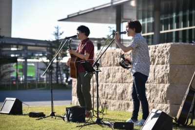 三田市内の屋外会場で左側の男性はギターを弾き右側の男性はタンバリンを叩いてライブをおこなっている写真