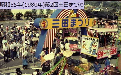 昭和55年におこなわれた第2回三田まつりのおまつり広場でロゴマークが描かれたバルーンアーチから出発する花車を眺める人々の写真