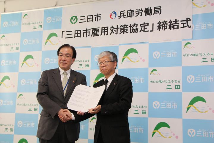 三田市役所の市長公室にて行われた三田市雇用対策協定の締結式にて三田市の人と兵庫労働局の人が並んで握手をしている様子の写真
