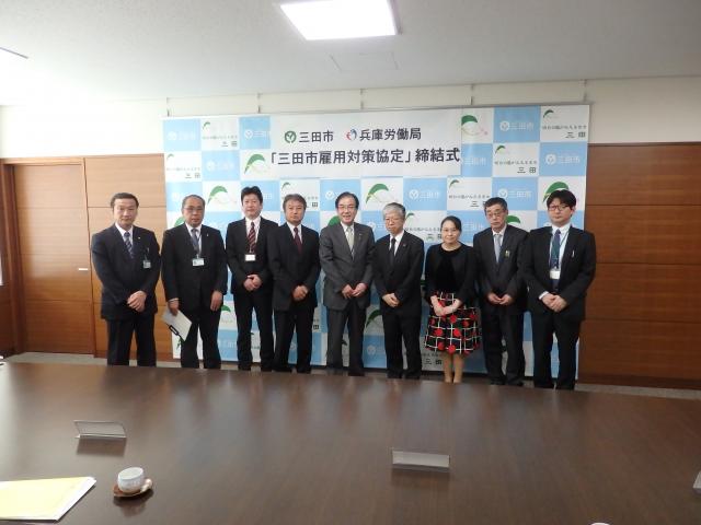 三田市役所の市長公室にて行われた三田市雇用対策協定の締結式にて三田市と兵庫労働局の人々9人が並んで立っている様子の写真