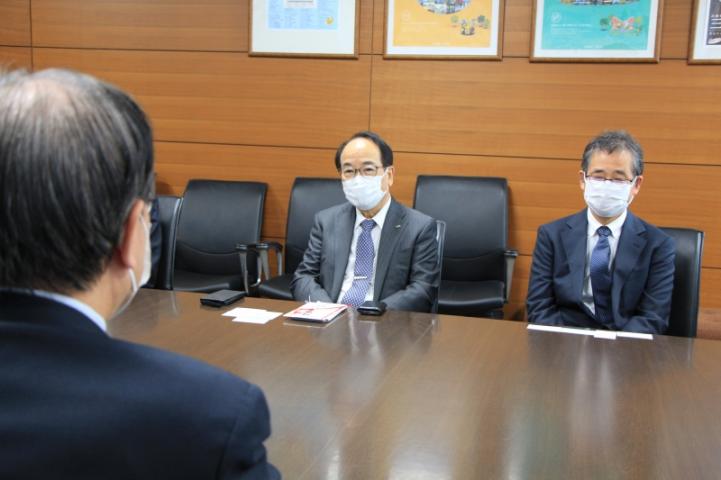 三田市役所市長公室で茶色の横長会議机で上木社長と向かい合って会話をする森市長を背中側から撮影した写真