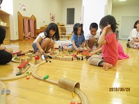 「親子サロン」のスペースで汽車と線路のオモチャで遊ぶ子供達の写真