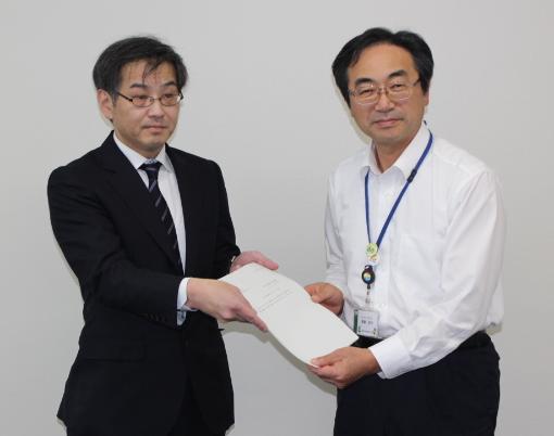 スーツを着た男性と、白いワイシャツを着た男性が、書類を受け渡している写真