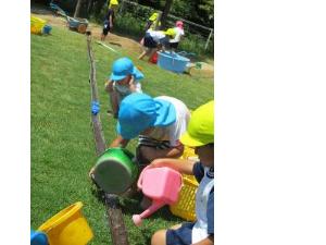 園児が砂場で樋をつないで水流しを楽しんでいる写真